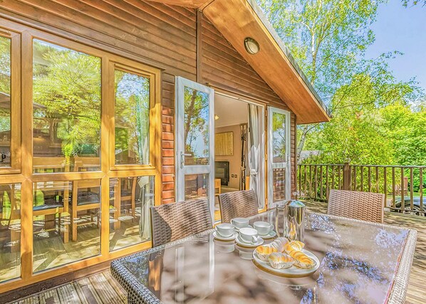 A wooden cabin with large windows, a glass dining table, and outdoor seating.