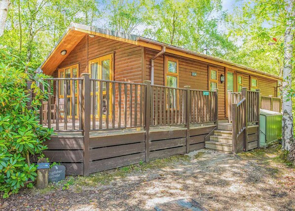 A wooden cabin with a deck, surrounded by trees.