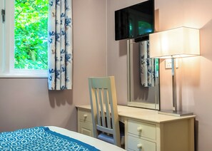 A bedroom with a bed, a dresser, a chair, a TV, and a window with curtains.