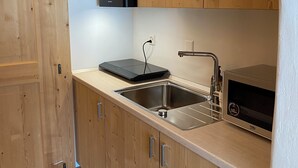 Cocina compacta con armarios de madera, microondas integrado y pileta de acero inoxidable.