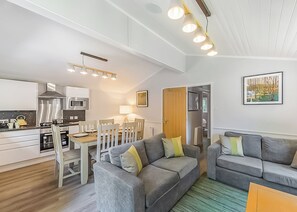 A modern living room with a grey sofa, a dining table, and a kitchen area with a microwave and oven.