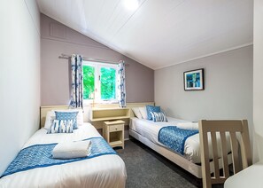 Quarto duplo com duas camas, uma escrivaninha, uma cadeira e uma janela com cortinas.