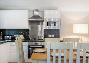 A modern kitchen with white cabinets, a stainless steel range hood, an oven, a microwave, and a dining area with a table and chairs.