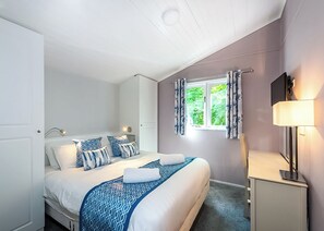 A bedroom with a bed, a bedside table, a lamp, a window with curtains, and a door.
