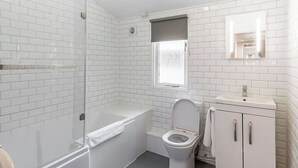 Ein Badezimmer mit weißen Fliesen, einer Badewanne, einer Toilette und einem Waschbecken mit Spiegel.