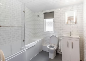 A bathroom with white tiled walls, a bathtub, a toilet, and a sink with a mirror above it.