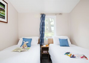 A bedroom with two beds, a window with a curtain, a nightstand with a lamp, and a framed picture on the wall.