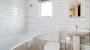 Ein modernes Badezimmer mit weißen Fliesen, einer Badewanne, einer Toilette und einem Waschbecken.