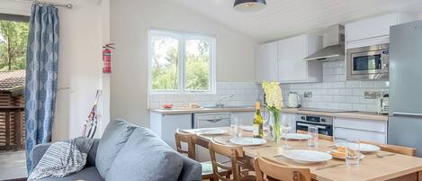 Una cocina moderna con armarios blancos, una mesa de comedor preparada para cuatro personas y un sofá gris en la sala de estar.