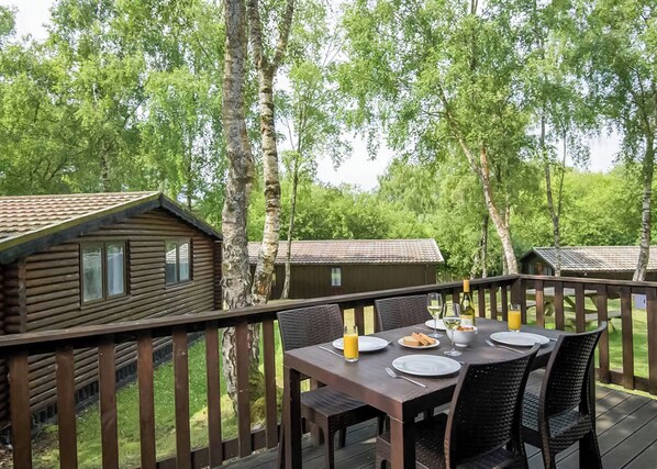 A wooden deck with a table set for breakfast, surrounded by birch trees.