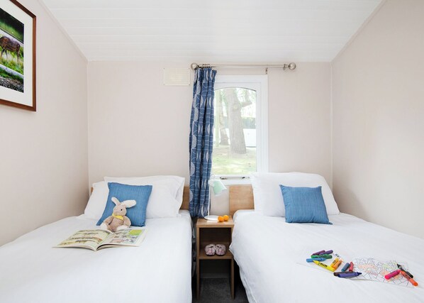 A bedroom with two beds, a window with a curtain, a nightstand with a lamp, and a framed picture on the wall.