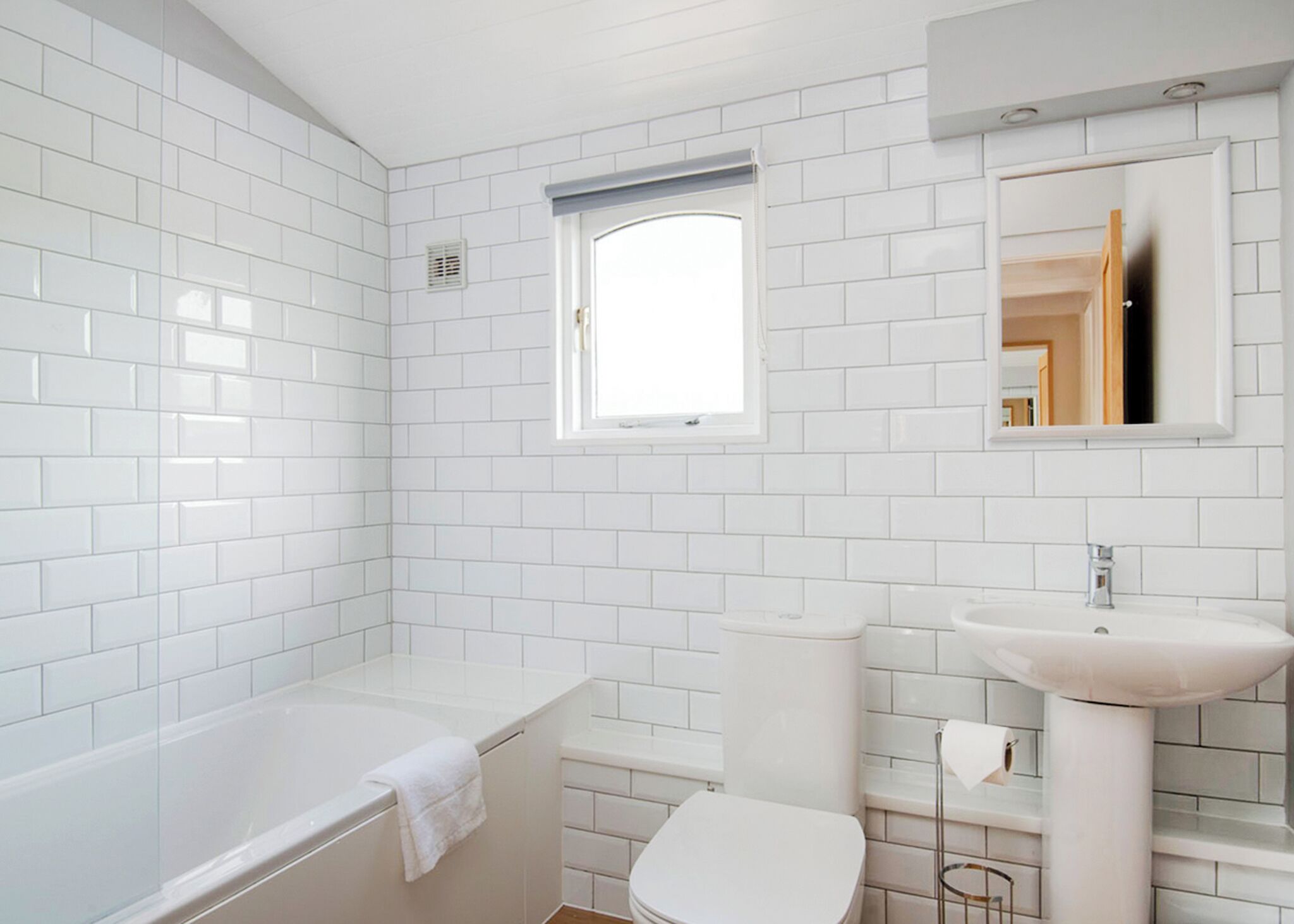 A modern bathroom with white tiles, a bathtub, a toilet, and a sink.