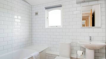 A modern bathroom with white tiles, a bathtub, a toilet, and a sink.