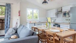 A modern kitchen with white cabinets, a dining table set for four, and a grey sofa in the living area. - Superior 3, Slps 8, parking, decking, lake view (Near Weymouth)
