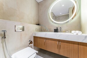 Ein modernes Badezimmer mit Marmorwaschtisch, rundem Spiegel mit LED-Beleuchtung, Dusche und Toilette.