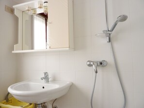 A bathroom with a white sink, a mirror above it, and a shower with a handheld showerhead. - Functional apartment just steps from the beach (Bibione Pineda)