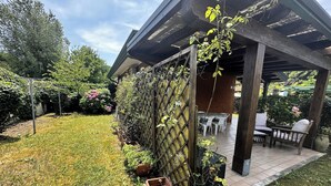 Un patio cubierto con una mesa y sillas, rodeado de un jardín con diversas plantas y una valla de madera.