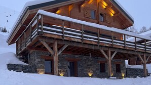 Eine Holzhütte mit Steinunterbau, umgeben von Schnee, mit Balkon und mehreren Fenstern.