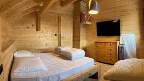Ein Zimmer in einer Holzhütte mit einem Bett, einem Schminktisch und einem Fernseher.