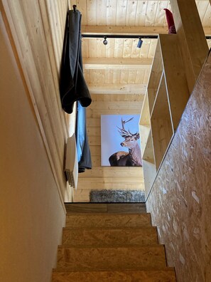 Una escalera de madera que lleva a una habitación con techo de madera y un cuadro enmarcado de un ciervo.