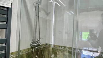 Een douchecabine met glazen wanden, een handdouche en een kraan op de muur.