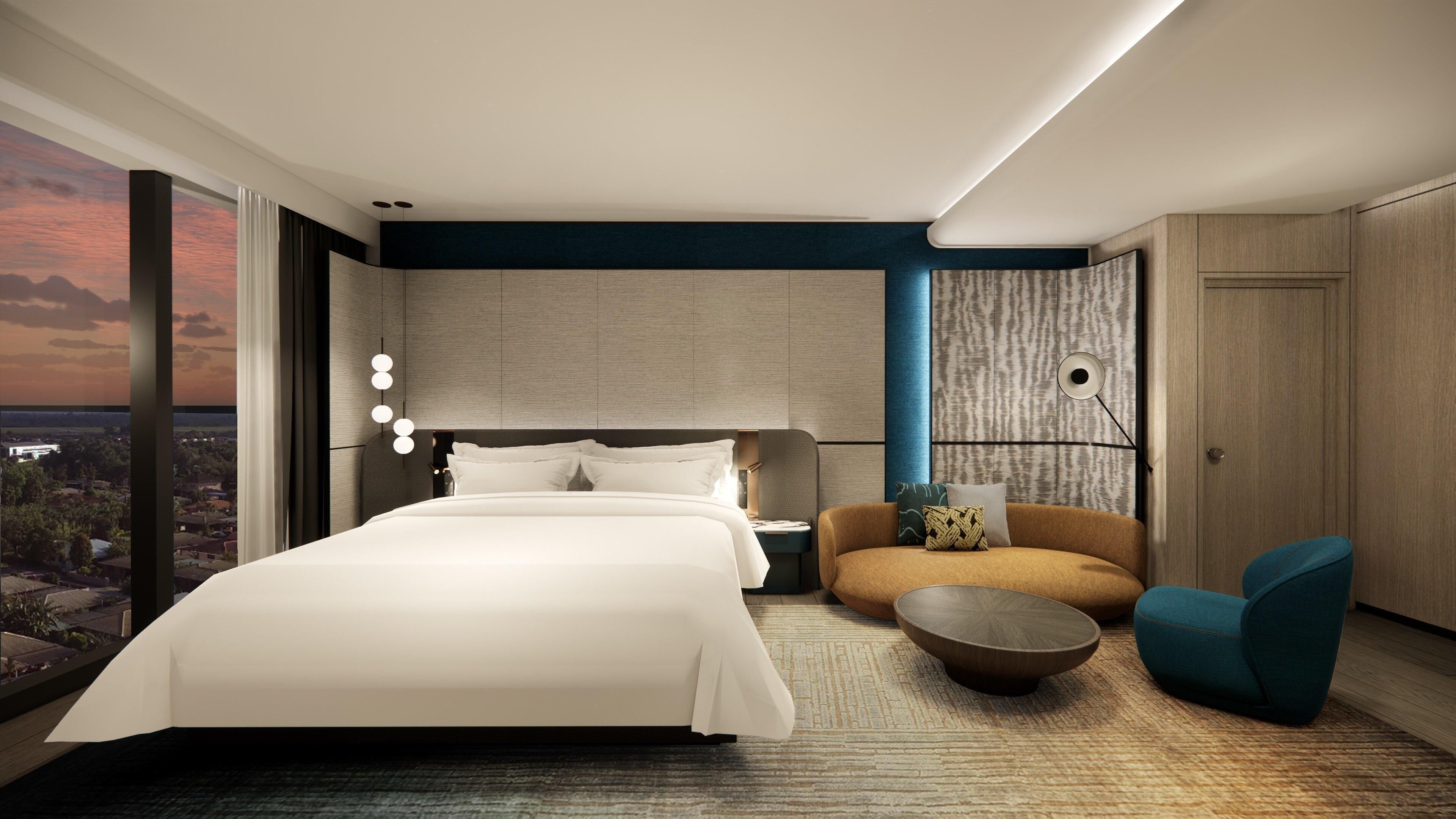 A modern hotel room with a large bed, a seating area with a coffee table, and a view of the cityscape.