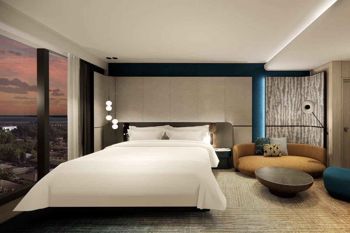A modern hotel room with a large bed, a seating area with a coffee table, and a view of the cityscape.