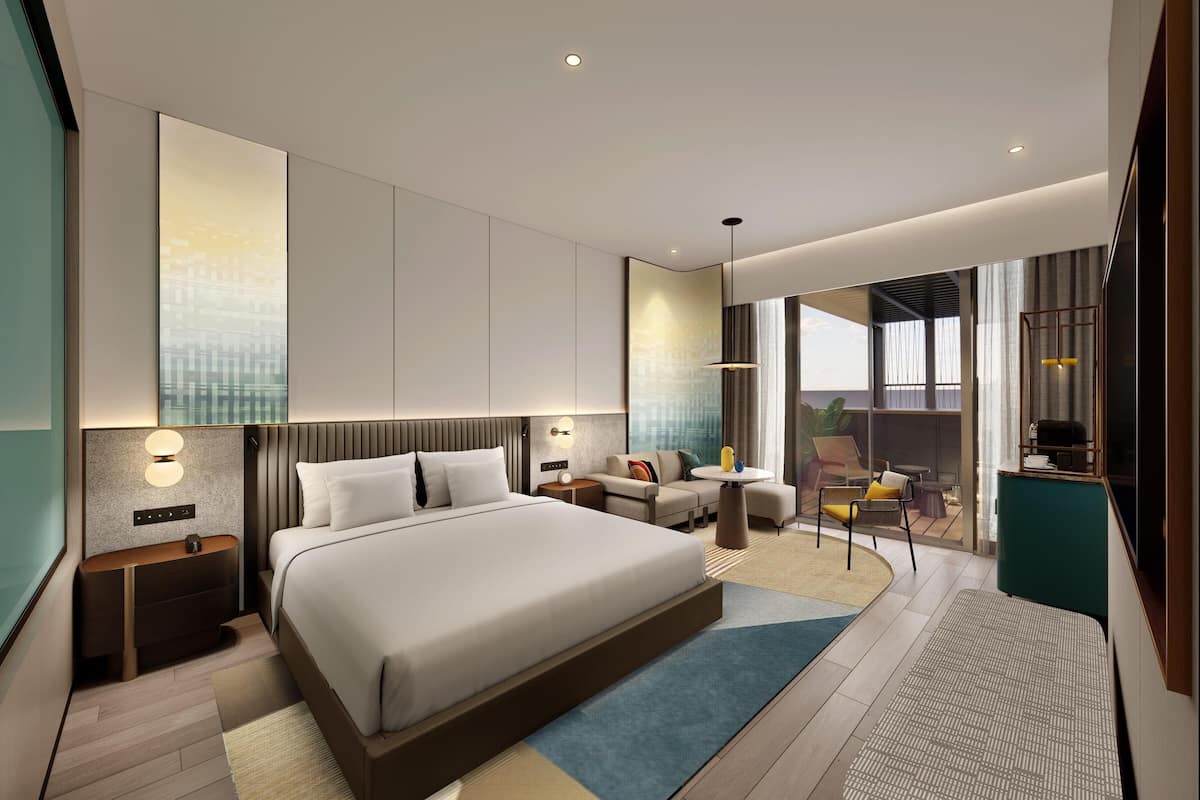 A modern hotel room with a large bed, a sitting area with a small table and chairs, a balcony with a view, and a TV on a stand.