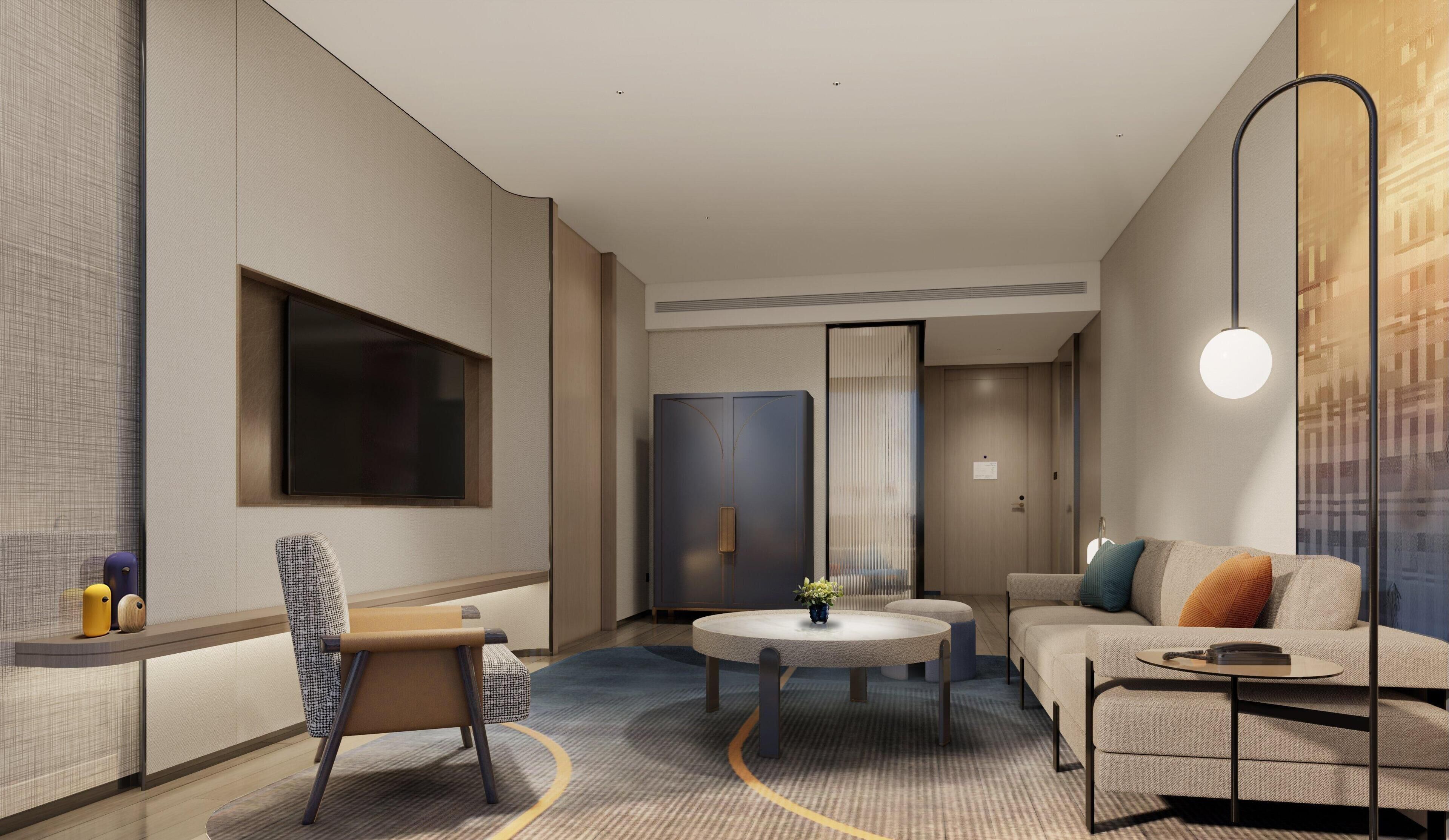 A modern hotel room with a sofa, a round table, a chair, a TV, and a wardrobe.