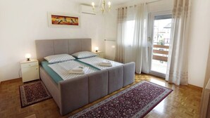 Een slaapkamer met een bed, nachtkastjes, een kroonluchter, een schilderij en uitzicht door een raam.