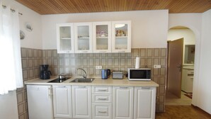 Een kleine keuken met witte kasten, een spoelbak, een koffiezetapparaat, een broodrooster en een magnetron.