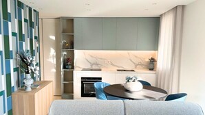 Una sala moderna con un sofá gris, una mesa de comedor con sillas, una zona de cocina con salpicadero de mármol y una estantería.