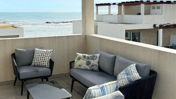 Un balcón con sofá, sillas, una mesita y vista al mar.