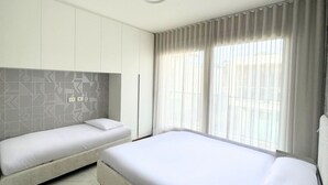 Habitación de hotel con dos camas, un cabecero de estampado geométrico, un ventanal con cortinas y un techo blanco.