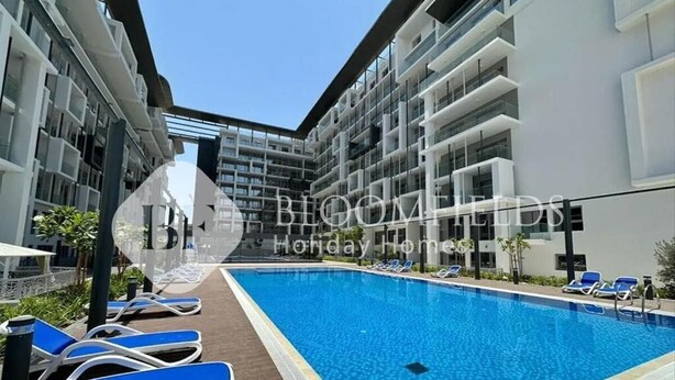 A modern hotel with a central swimming pool, lounge chairs, and a clear sky. - Bloomfields Pretty Stu in Oasis  (Abu Dhabi)
