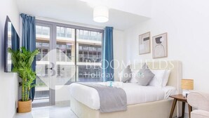 A modern hotel room with a large bed, a small table, a potted plant, and a view of the city through the window. - Bloomfields Pretty Stu in Oasis  (Abu Dhabi)