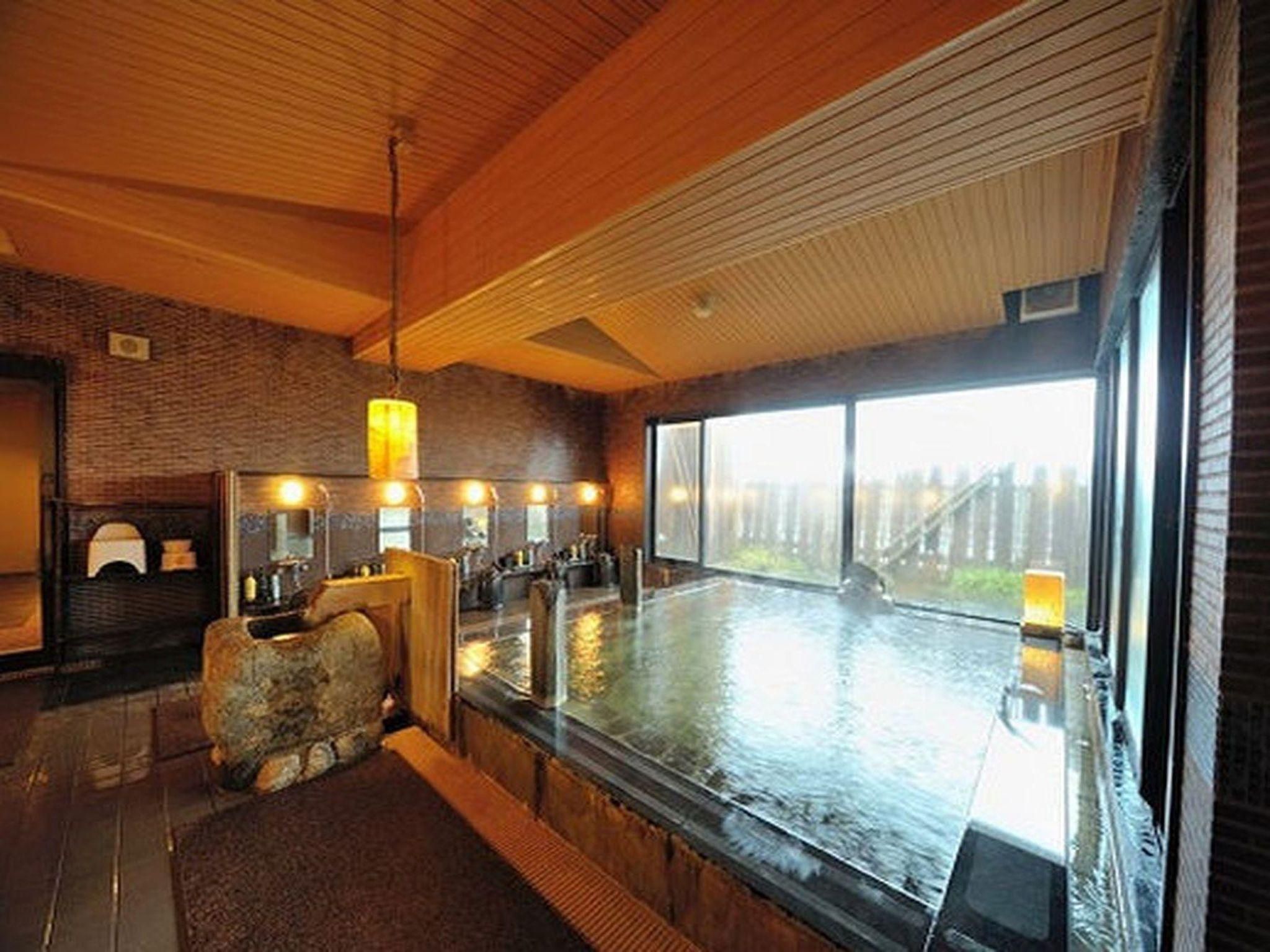 A hot spring bath area with wooden beams, a stone seating area, and a view of a bridge outside.