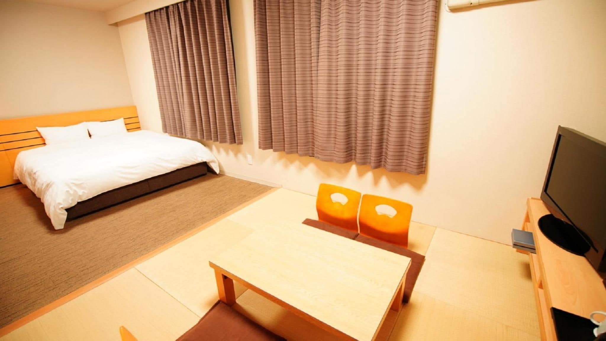 A hotel room with a bed, a desk, a television, and curtains.