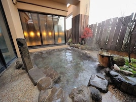 Zona de aguas termales con un baño de piedra rodeado de rocas y una valla de madera.