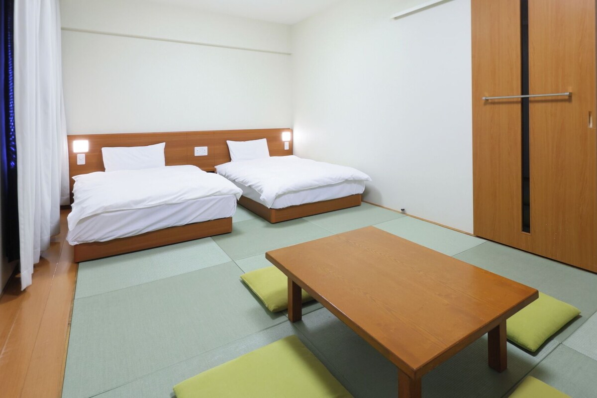 A hotel room with two beds, a wooden table, and a wardrobe.