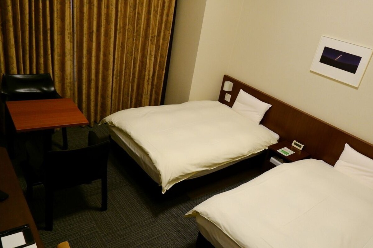 A hotel room with two beds, a desk, and a chair.