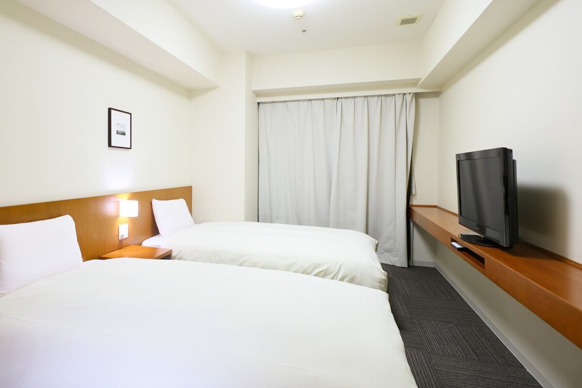 A hotel room with two beds, a TV, a picture on the wall, and a window with curtains.