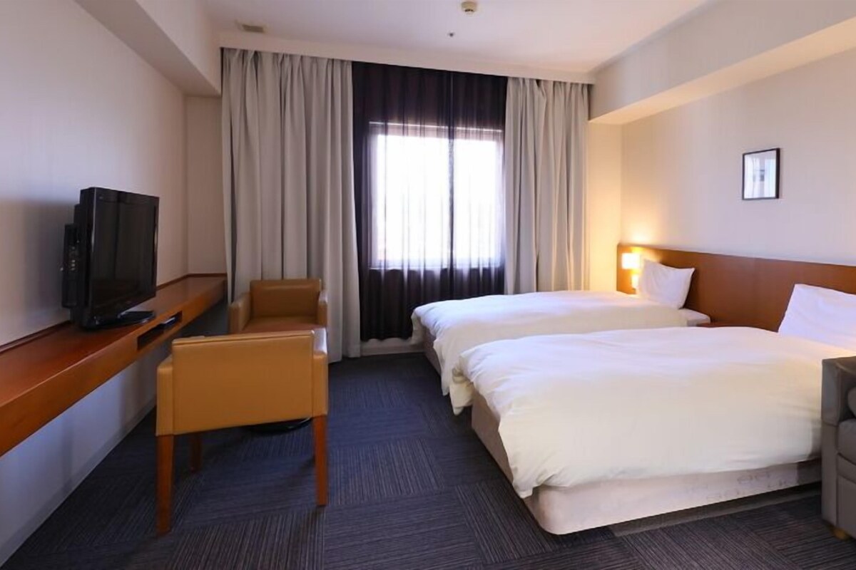 A hotel room with two beds, a desk with a television, a chair, and a sofa.