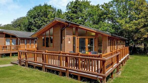 Una cabaña de madera con terraza, ventanas grandes y un patio con césped.