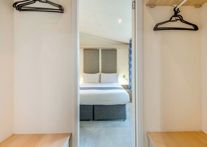 A hotel room with a bed, a bedside table, and a wardrobe with a mirror. - Superior Lodge with ensuite & decking (Near Weymouth)