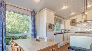 A kitchen with a dining table, chairs, a microwave, and a trash bin. - Superior Lodge with ensuite & decking (Near Weymouth)