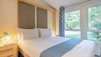 Une chambre d’hôtel avec un lit, une table de chevet, une lampe et une fenêtre donnant sur un paysage verdoyant.