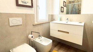 Un baño moderno con bidé, un porta papel higiénico y un espejo grande sobre el lavabo.