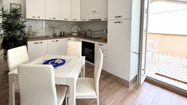 Una cocina moderna con armarios blancos, una mesa de comedor con sillas y vistas al exterior.