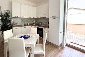 Une cuisine moderne avec des meubles blancs, une table à manger avec des chaises et une vue sur l’extérieur.